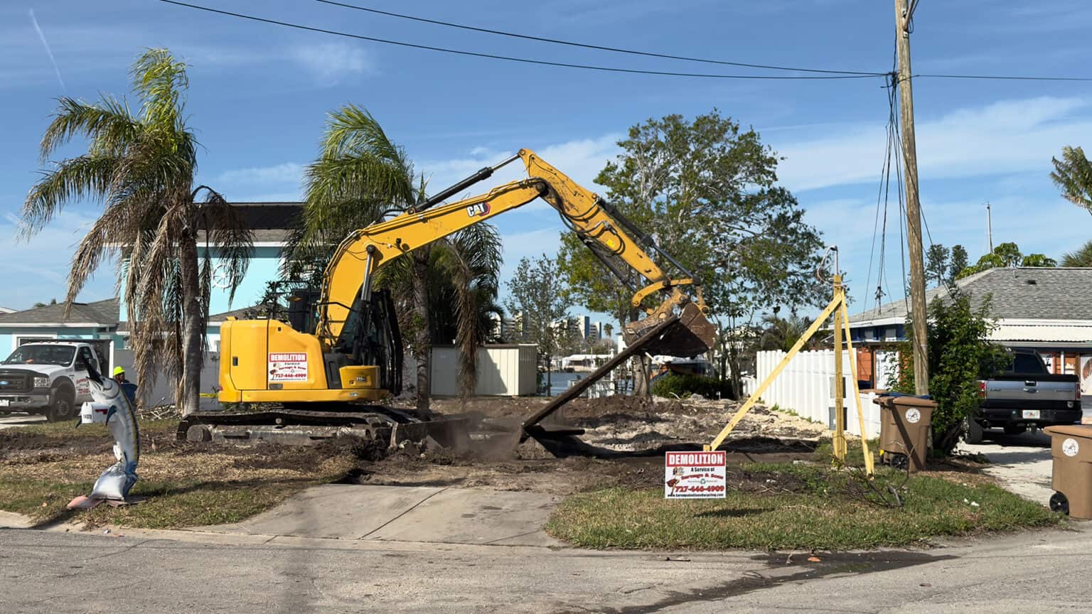 CAT mini-excavator pulling up a residential driveway slab beside a Sarnago demolition yard sign