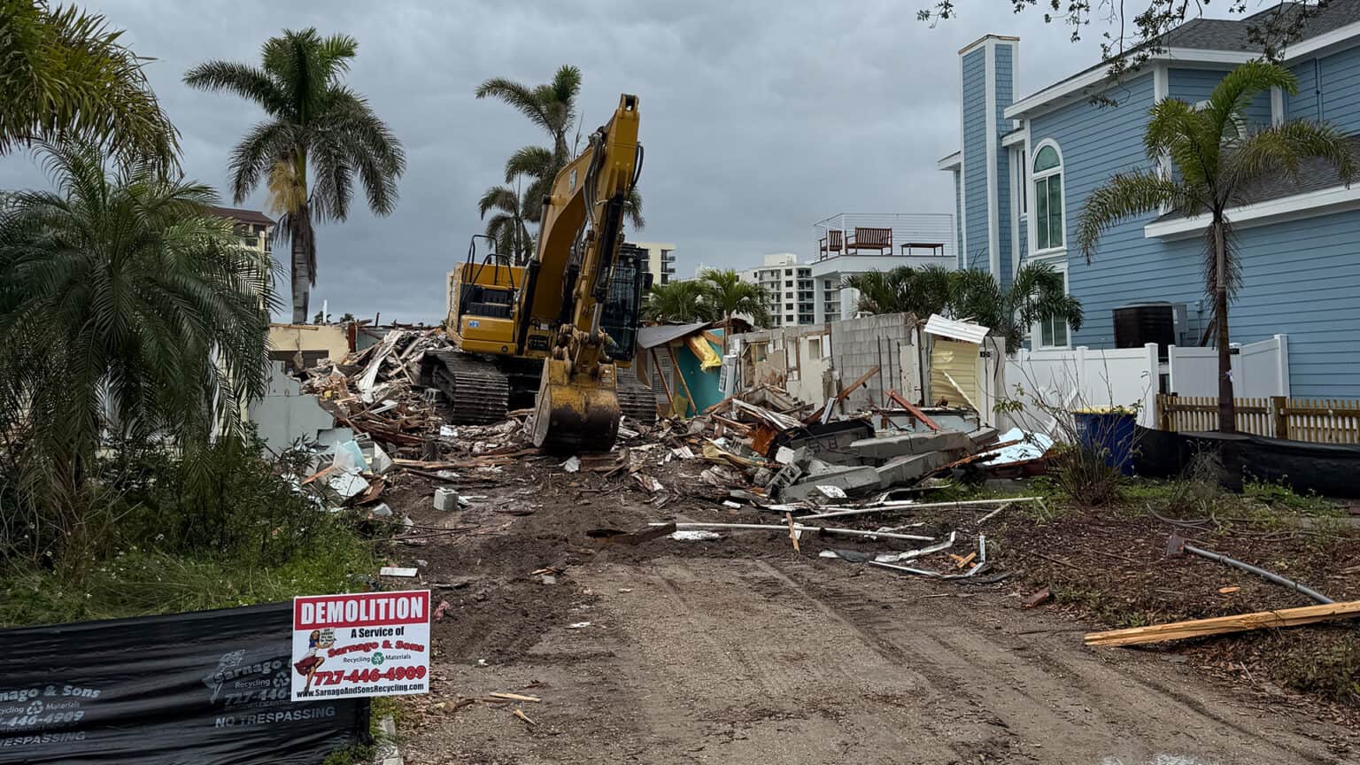 Excavator working the last rubble pile on a cleared coastal lot behind a Sarnago & Sons site sign